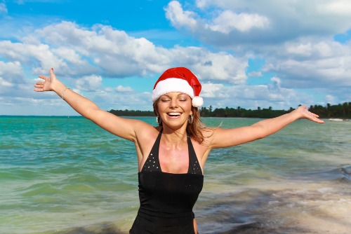 Christmas in Maui: A woman wearing a Santa hat gleefully raises her arms amid a beautiful beach in West Maui during a Christmas vacation.